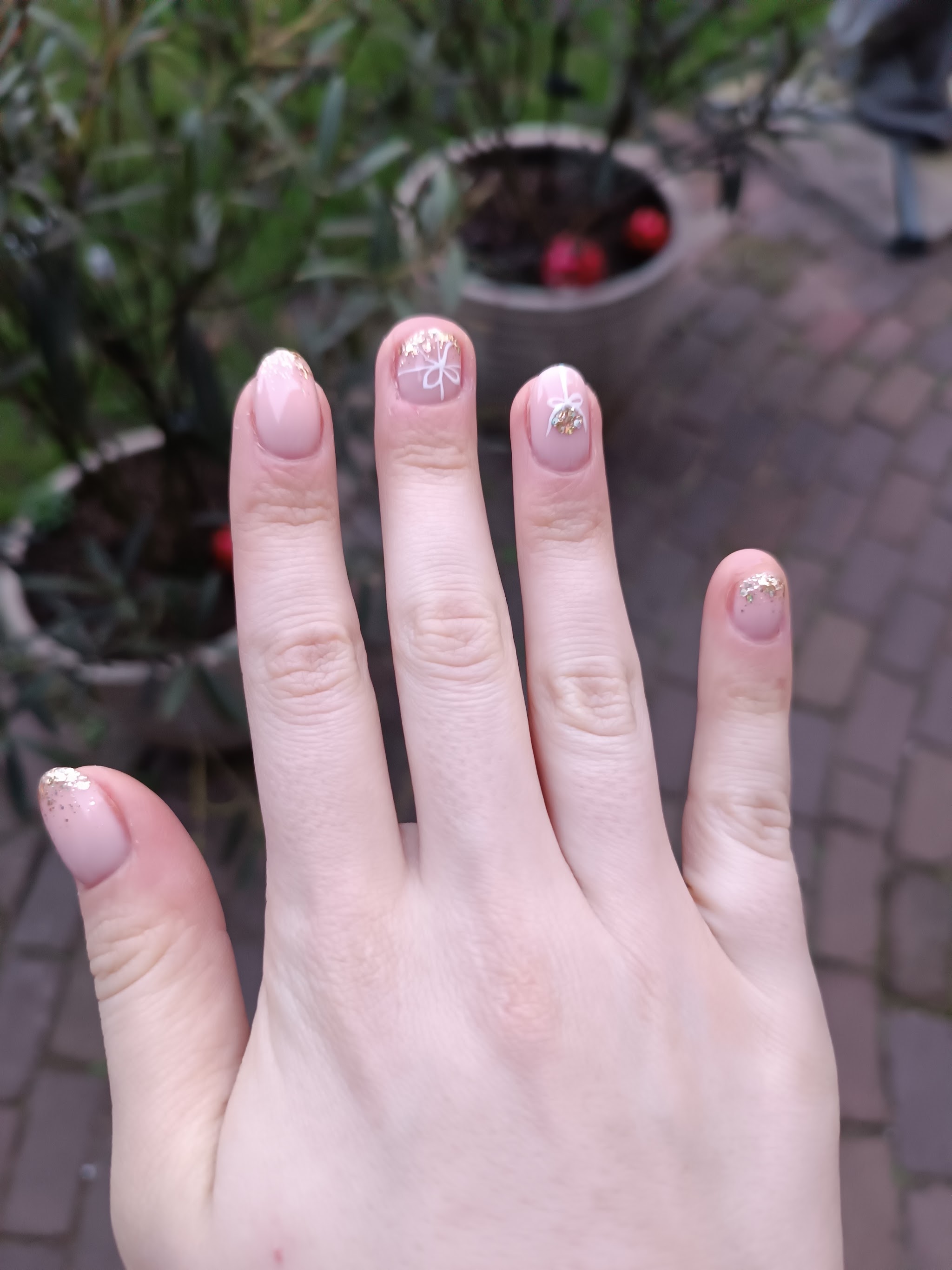 Nagels van Daniëlle met gouden glitters en witte strikjes, gefotografeerd in de tuin